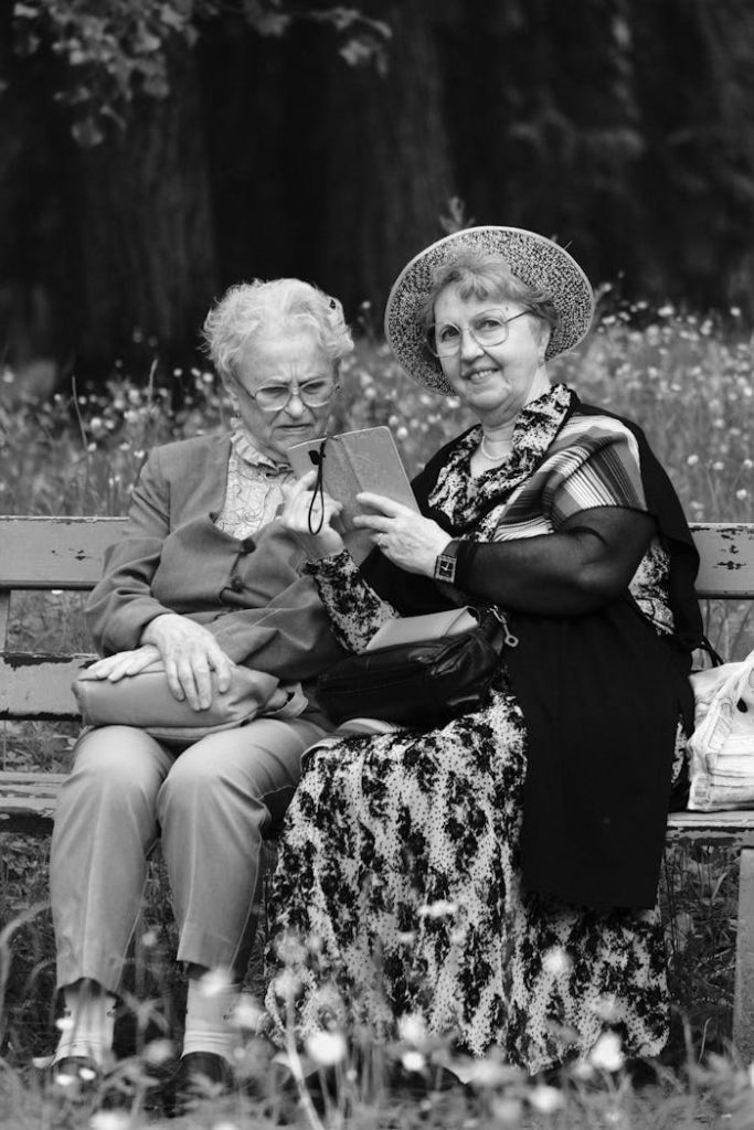 Two senior women sitting on a park bench sharing a joyful moment outdoors.